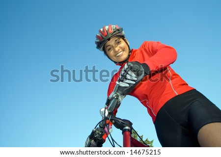 Close-up of woman standing next to bicycle, looking down and smiling. Wearing sports gear and helmet. Horizontally framed shot.