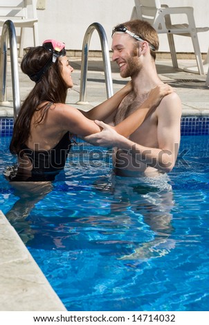 A man and woman are standing together in a pool.  They are hugging and looking at each other.    Vertically framed photo.