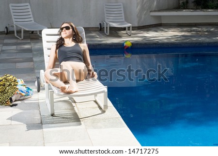 An attractive woman, lying in a pool chair, relaxing at the poolside - horizontally framed