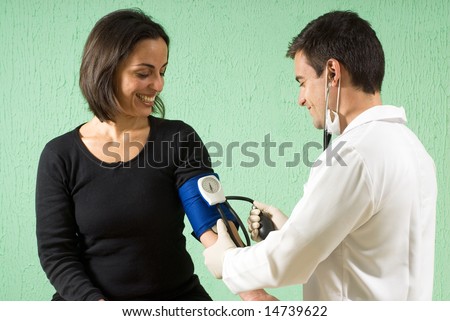 A young, male doctor is checking the blood pressure of a smiling patient.  The patient and the doctor are both looking down at her arm.  Horizontally framed photo.