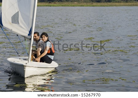 Smiling man and woman sitting on sailboat sailing across lake. Horizontally framed photo
