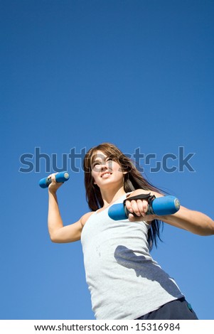 An attractive, fit woman is working out with hand weights.  She is smiling and looking away from the camera.  Vertically framed shot.