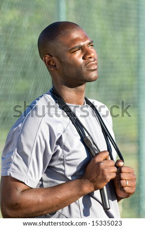 A young, attractive man is standing on the tennis court holding jump ropes around his neck. Vertically framed shot.