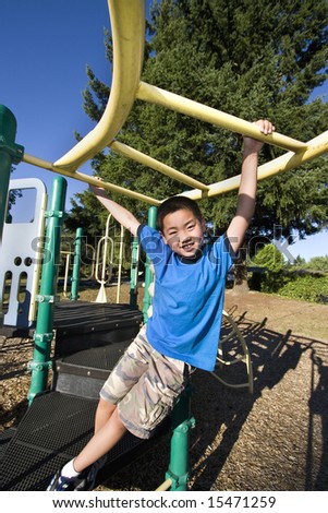 Young Asian boy climbing on jungle gym. He is smiling at camera. Vertically framed photo.