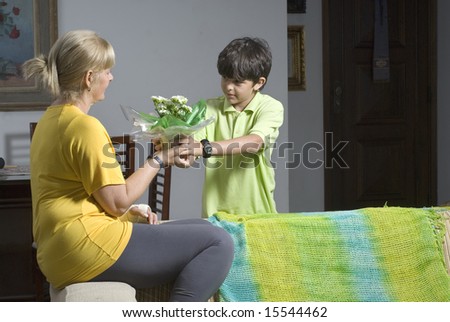 A child is presenting flowers to his mother.  They are looking at each other.  Horizontally framed shot.