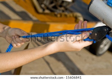 Close up shot of a woman\'s hand as she fixes the sail on her sailboat.  She is pulling on the ropes.  Horizontally framed shot.