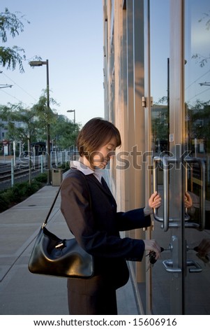 A woman, standing in front of two large glass doors, unlocking them. away from the camera. Vertically framed shot.