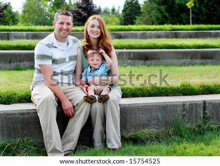 A young family is sitting together on a step. They are smiling at the camera.  Horizontally framed shot.