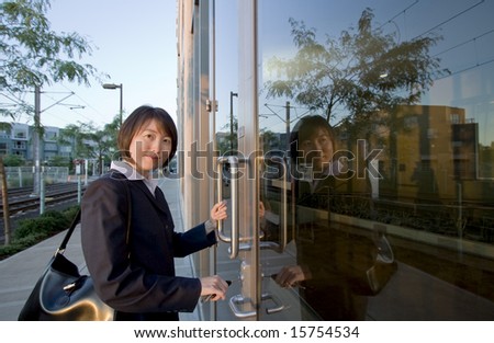 A woman, after unlocking two large glass doors, smiles at the camera, standing. Horizontally framed shot.