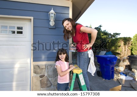 Mom and daughter smiling as they paint the house.. Horizontally framed photograph