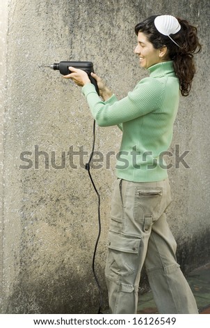 Woman with mask on head drills hole into wall with electric drill. Vertically framed photo.
