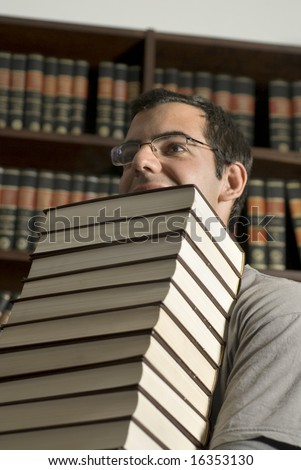Man with glasses carries a stack of books through a library. Vertically framed photo.
