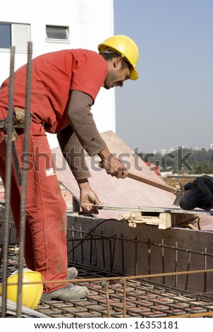 Construction worker wearing orange suit uses hammer on worksite. Vertically framed photo.