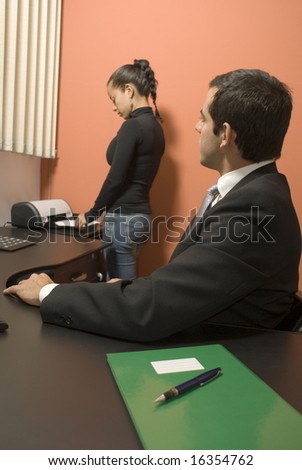 Businessman watches his secretary use the fax machine while sitting at his desk. Vertically framed photo.