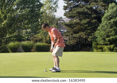 Man lines up his putter to putt the golf ball. Horizontally framed photo.