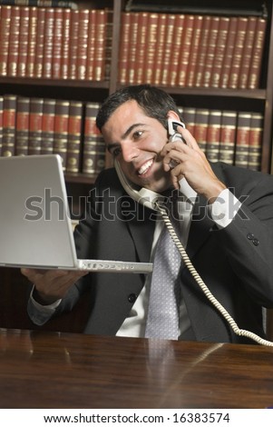 Smiling man in suit talks on two phones while holding laptop. Vertically framed photo.