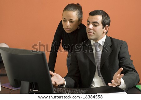 Businessman and woman at desk looking at a computer. He is looking surprised with his hands up. Horizontally framed photo