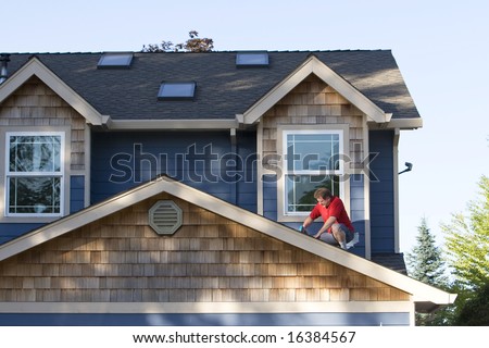 A man, kneels on his roof, looking down, drilling a hole in his roof, fixing the shingles. Horizontally framed shot.