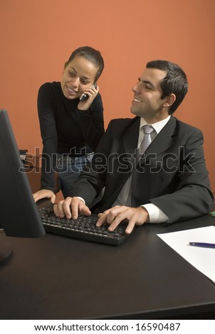 Businessman at his computer looks at his employee as she talks on a cell phone. Vertically framed photo.
