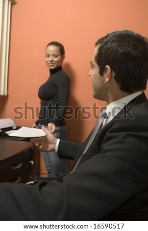 Businessman seated at desk while his co-worker shows him paperwork. Vertically framed photo.