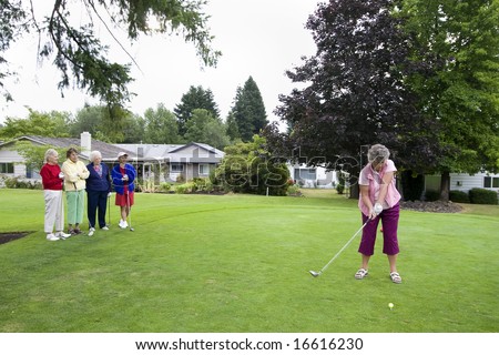 Elderly woman teeing off on the golf course as her four friends watch. Horizontally framed photo.