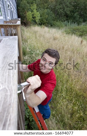 Man with a silly smile on his face standing on a ladder fixing a porch with a wrench. Vertically framed photo.