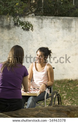 Young girl in wheelchair playing cards in with another girl. Vertically framed photo.