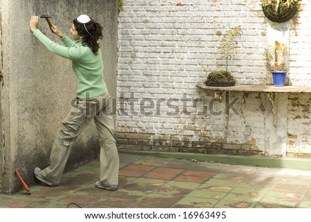 Woman hammers nail into wall. She is wearing a dust mask on her head. Horizontally framed photo.