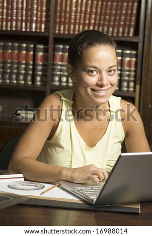 Smiling woman sitting at desk with laptop computer. Vertically framed photo.