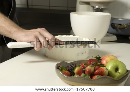 Hands using a knife to smooth out the icing on a cake. There is a fruit plate next to it. Horizontally framed photo.