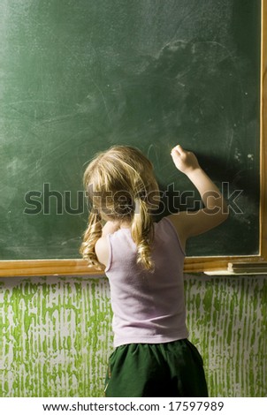 A little girl writing on a chalkboard.  Her back is to the camera.  Vertically framed shot.