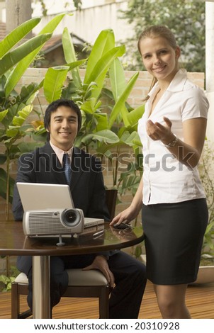 Smiling man and woman with a projector. He is seated and she is standing with her arm out. Vertically framed photo.
