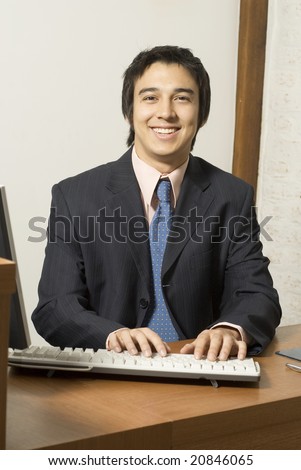Businessman at desk smiling while typing at a computer. Vertically framed photo.
