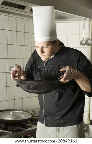Chef in kitchen smelling food in a wok. Vertically framed photo.