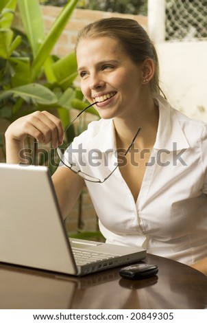 Smiling woman at a computer with her glasses between her lips. Vertically framed photo.