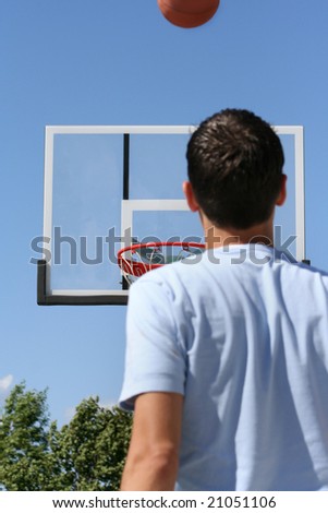 The rear view of a young boy facing a hoop as a basketball ascends toward it. Horizontally framed shot.