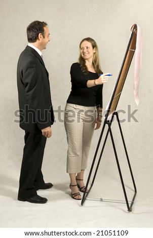 A man and a woman are standing in front of a large presentation board.  They are smiling at each other and the woman is about to write something on the board.  Vertically framed shot.