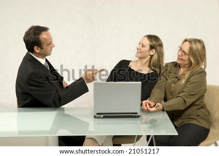 Boss pointing at his employees as they all sit at a desk in front of a computer. Horizontally framed photo.