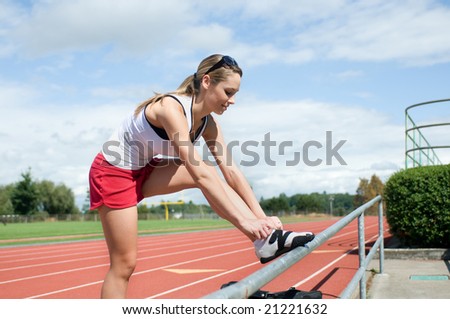 Woman leaning on a rail by the bleachers tying her shoe at a track. Vertically framed photo.
