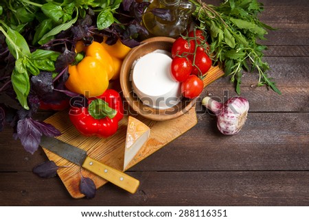 Bell peppers, basil, garlic, ricotta, goat cheese, tomatoes and arugula on a wooden table