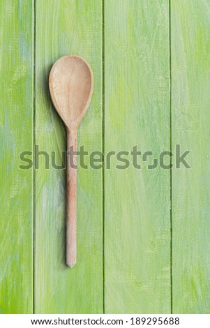 Wooden serving spoon with black peppercorns on green painted wooden surface