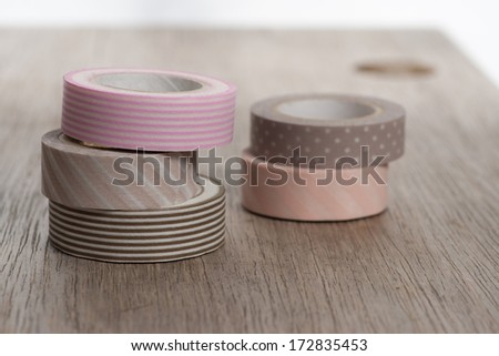Washi tape rolls, masking tape rolls in pile on wooden bench. Five tape rolls. light brown and beige tapes.