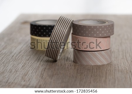 Washi tape rolls, masking tape rolls in pile on wooden bench. Six tape rolls. light brown and beige tapes.