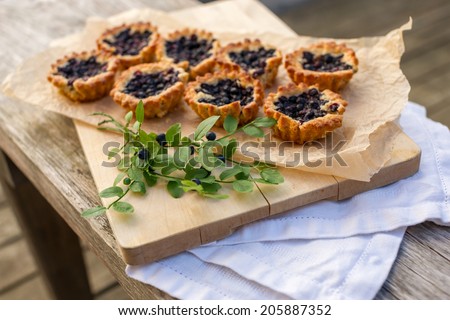 Eight small and fresh blueberry pies on wooden table. Bilberry pie on top of paper and linen. Fresh and tasty homemade blueberry pie.