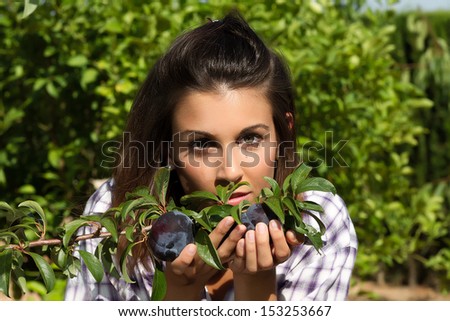 Beautiful young woman smelling ripe plums of the branch