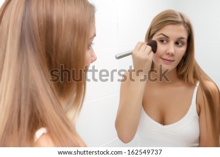 Beautiful young woman applying foundation powder or blush with makeup brush