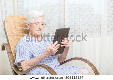 Old woman using a digital tablet on chair