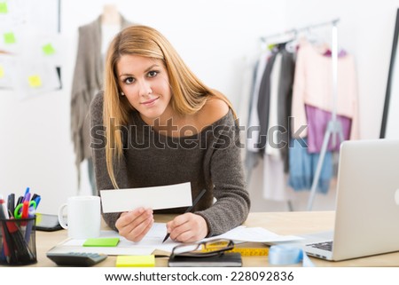 Young attractive female fashion designer leaning on office desk, working with a laptop