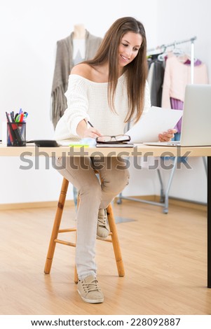 Young attractive female fashion designer leaning on office desk, working with a laptop