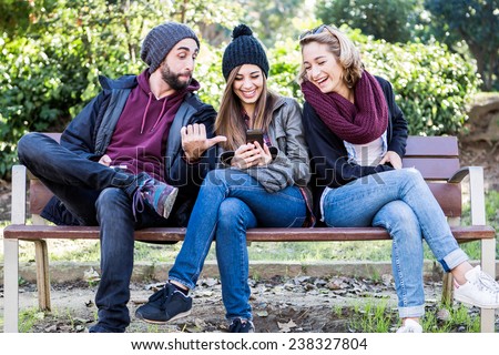Group of friends two women and one man, sitting on a bench in park